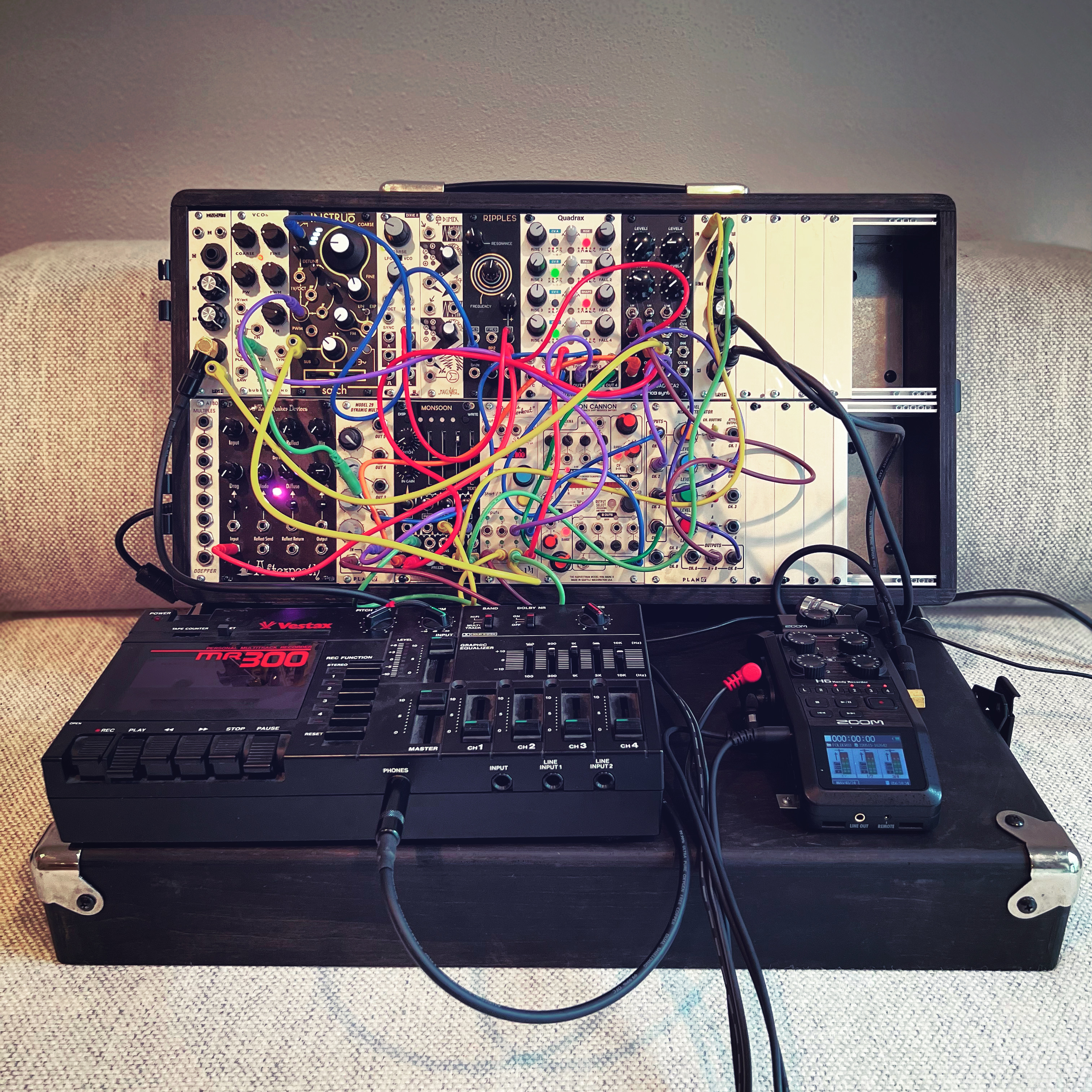 a modular synthesizer propped up on a couch, connected to a 4 track recorder and a digital multichannel recorder
