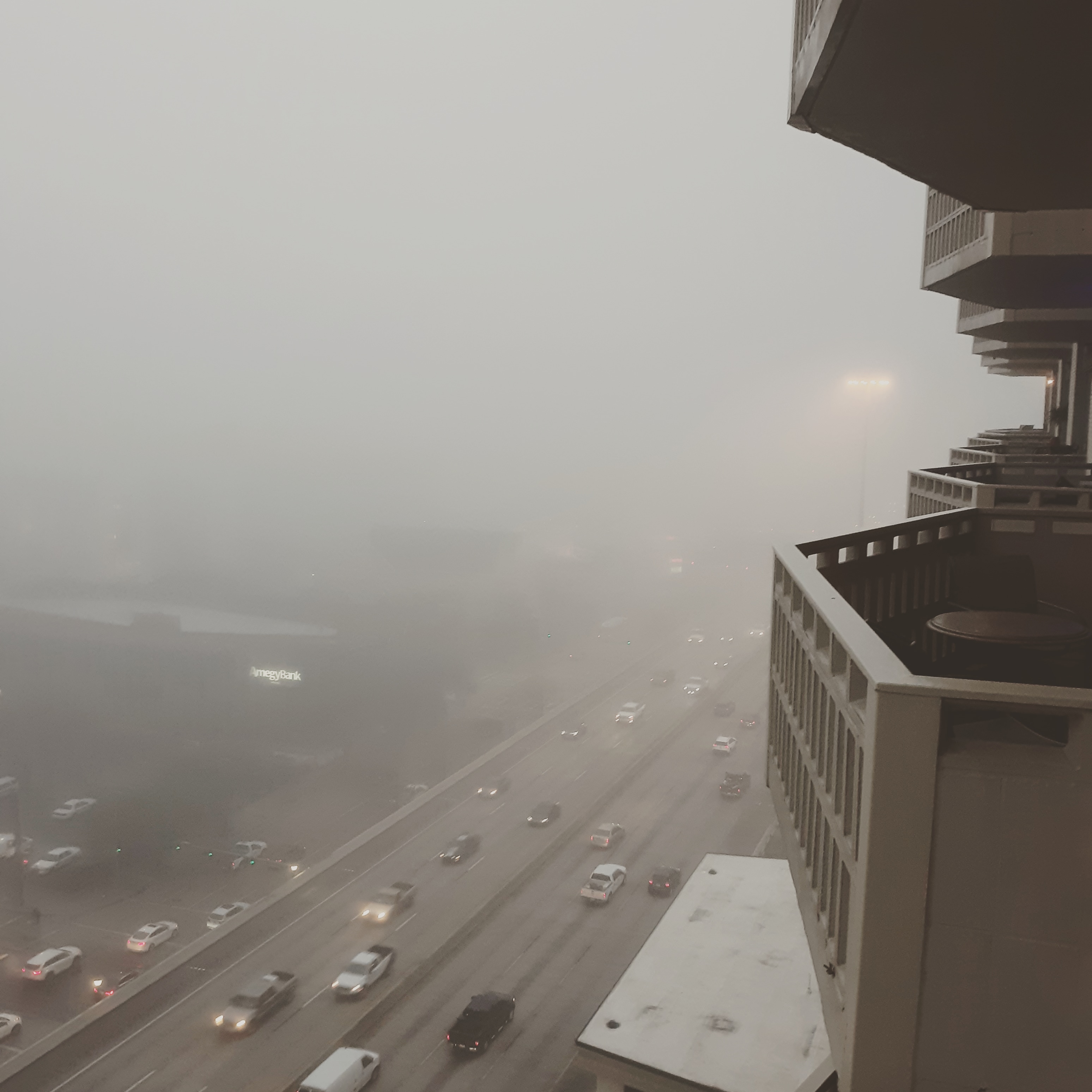 A photo of  Houston, Texas, shot from an apartment buildiing's balcony with consderable fog. Down and to the left, extending to the center, is a road with cars.